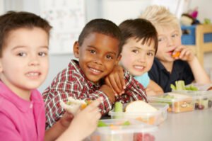 Group Of Elementary Age Schoolchildren Eating Healthy Packed Lunch In Class
